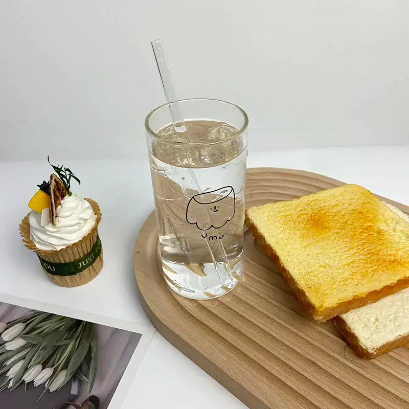 Clear glass cartoon glass cup with black line smiling face and yum text filled with ice water and clear plastic straw