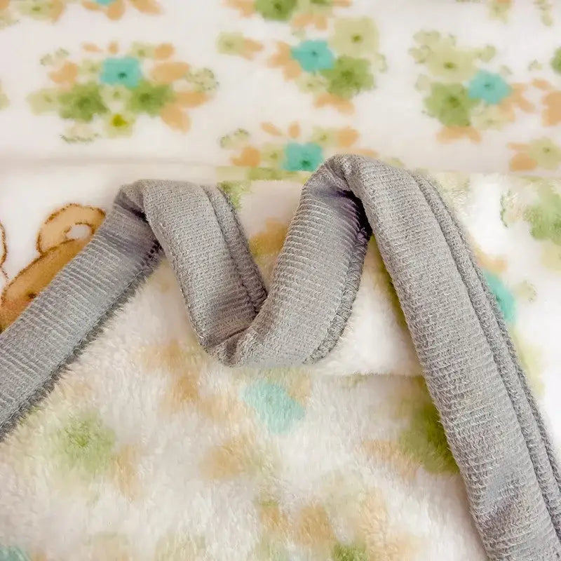 Gray ribbed fabric strap of decorbites cartoon milk velvet teddy bear blanket with soft plush texture and white floral design