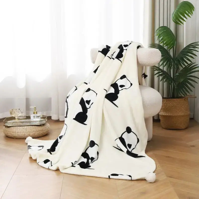 Cream-colored cartoon panda flannel white fleece blanket with black panda silhouettes and pom pom tassels for bedroom decorbites