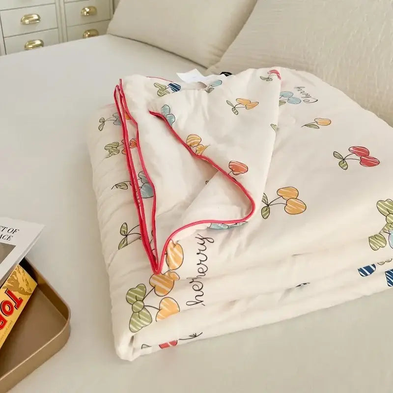 A soft off-white cartoon patchwork summer cooling blanket with colorful cherries hershey script and pink piping edges