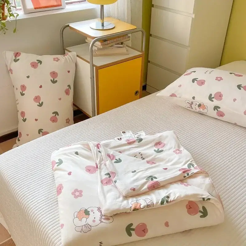 A folded white cartoon patchwork summer cooling blanket with pink cherry blossom and bunny pattern in soft cotton material