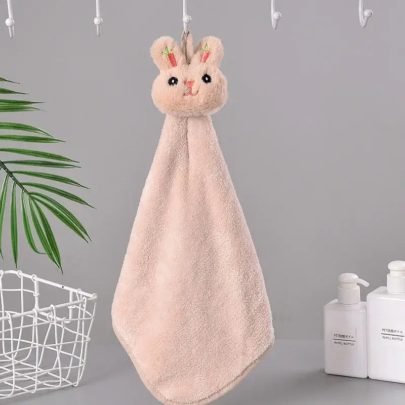 A soft pink cartoon rabbit coral fleece hand towel with embroidered carrot ears hanging on a hook for quick drying