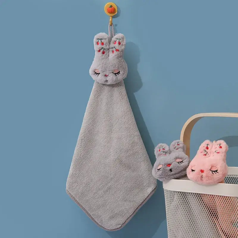 A soft gray coral velvet hand towel in the shape of a bunny with embroidered cheeks and closed eyes hanging on a hook decorbites cartoon rabbit