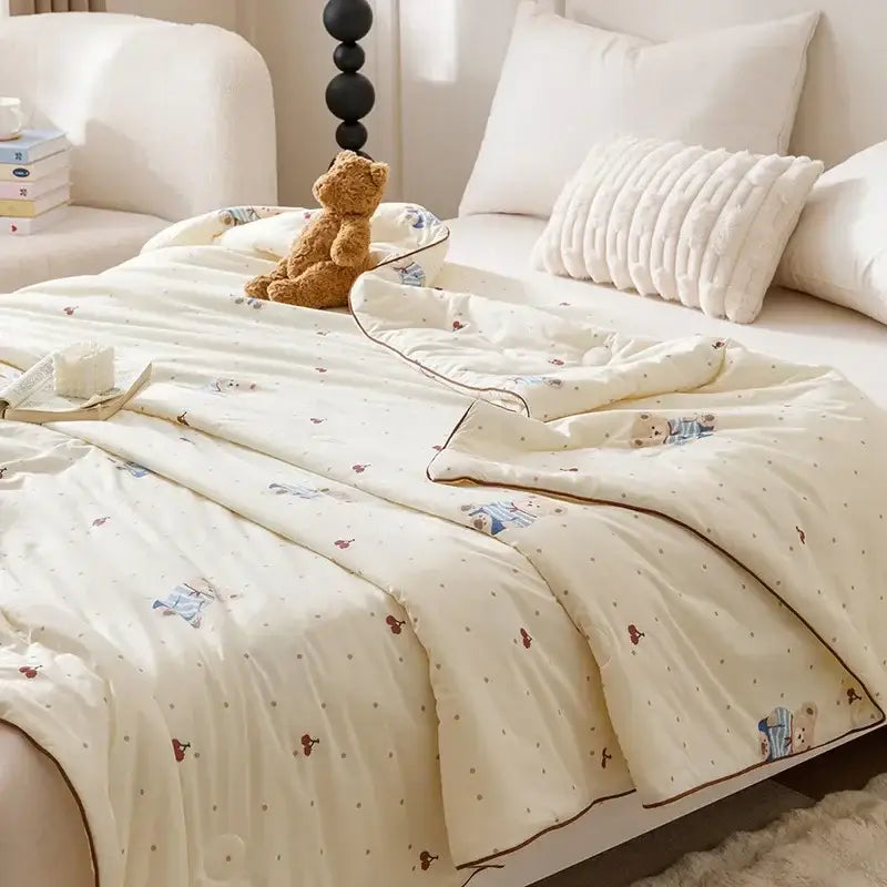Cream-colored quilted cooling summer blanket with plush texture and embroidered blue and brown teddy bear patterns