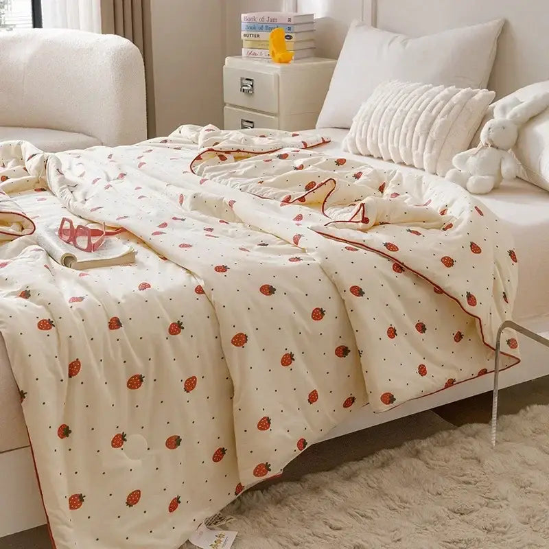 Cream-colored quilted cooling summer blanket with red strawberry prints and matching red border for bedroom use