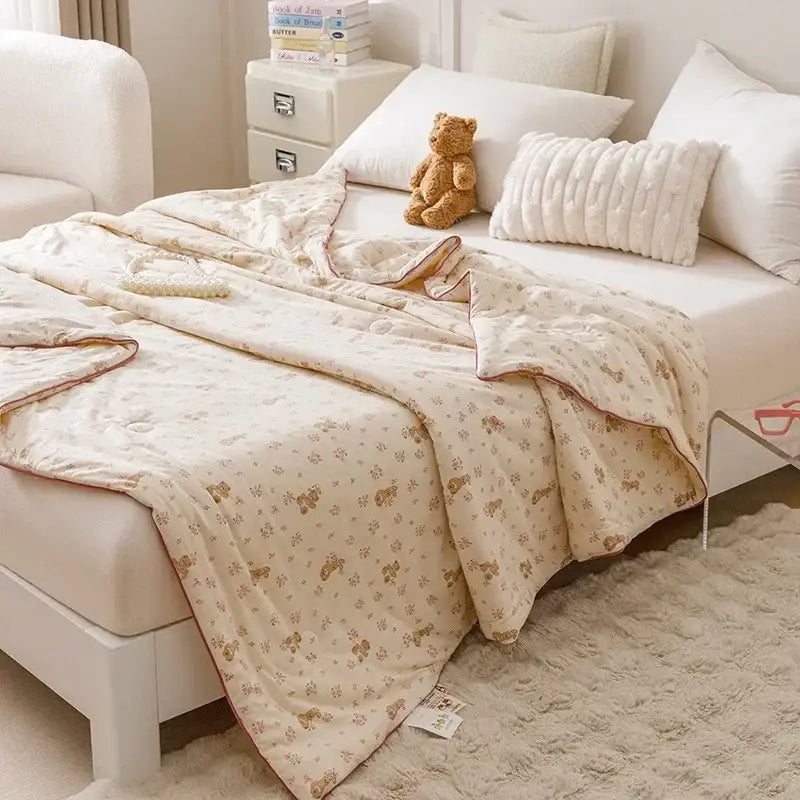 Cream-colored quilted cooling summer blanket with small brown teddy bear pattern and stitched edges for bedroom use