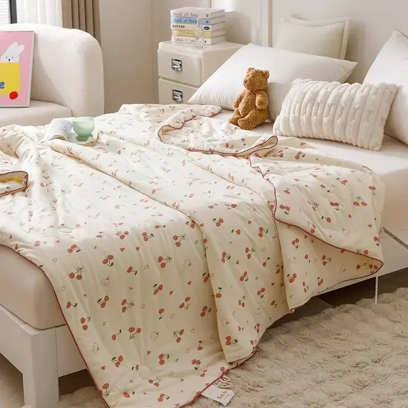 Cream-colored quilted cooling summer blanket with cherry and heart pattern and soft red edge stitching for bedroom use