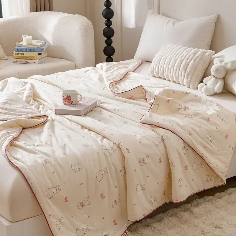 Cream-colored quilted cooling summer blanket with soft plush texture and delicate pink bunny prints for bedroom use