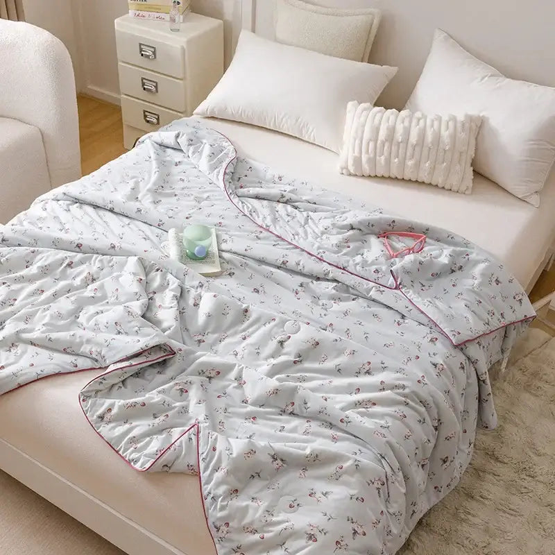 Cartoon rabbit off white cooling summer blanket with light blue floral pattern and pink piping draped over a bed