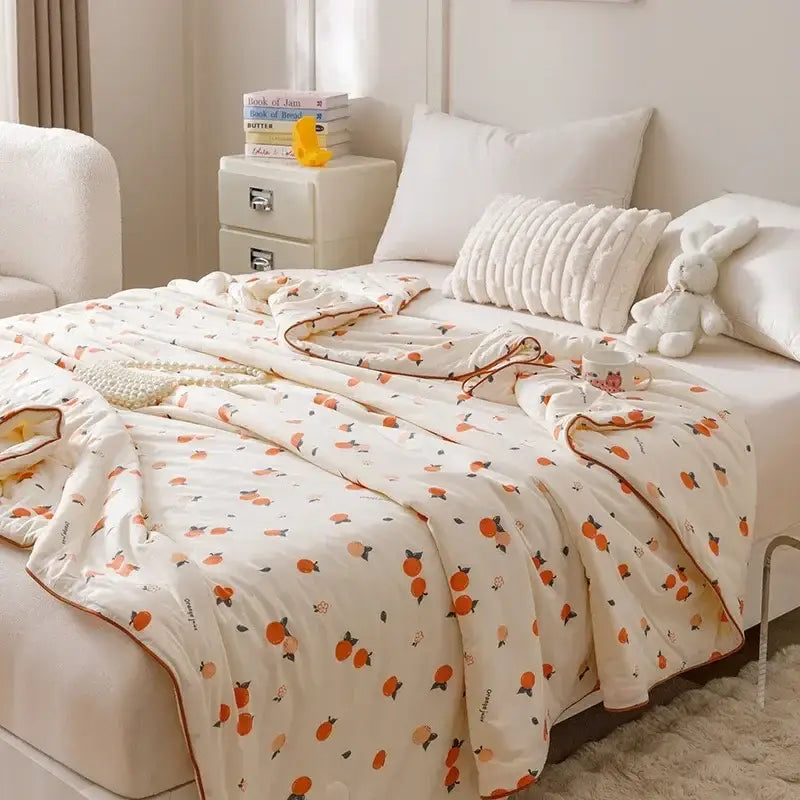 A soft off-white cooling summer blanket quilted with orange peaches and green stems, edged with thin brown piping