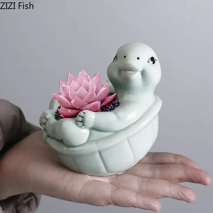 A light green cartoon turtle ceramic planter with a smiling face holding a pink lotus succulent for living room decor