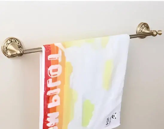 A white towel with orange yellow gradient stripe hanging from a carved antique bronze brass bathroom hardware set rack