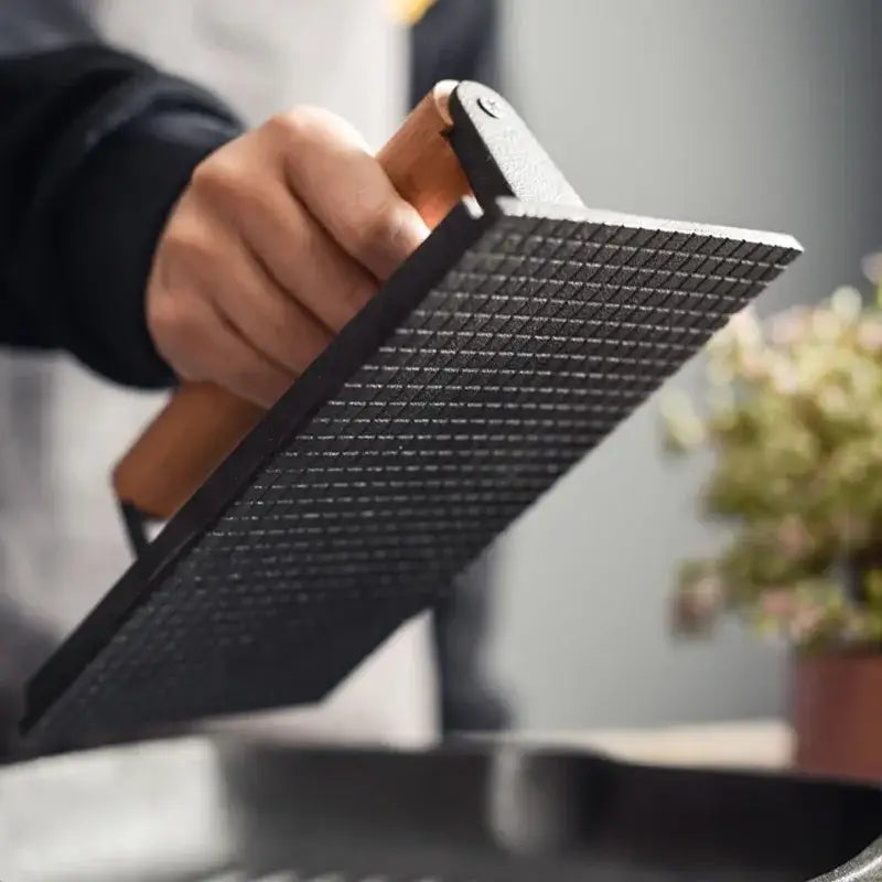 Black metal grater with wooden handle shown alongside cast iron steak press plate with grid pattern for kitchen use