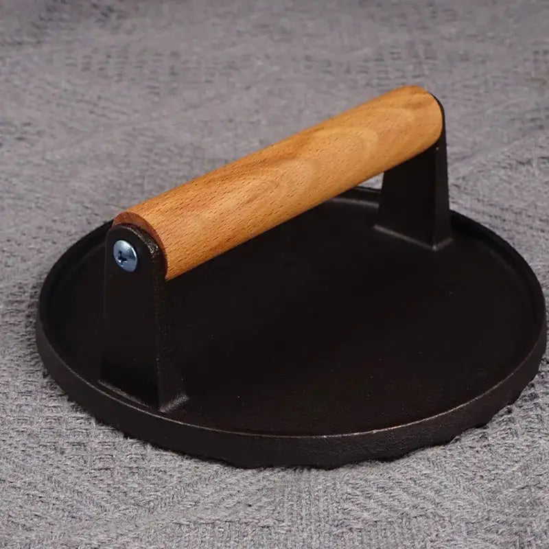 Black cast iron steak press plate with light brown wooden handle kitchen tool for grilling and pressing burgers
