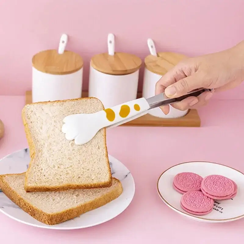 White silicone food tongs with yellow polka dots and cat paw design holding bread stainless steel kitchen gadget