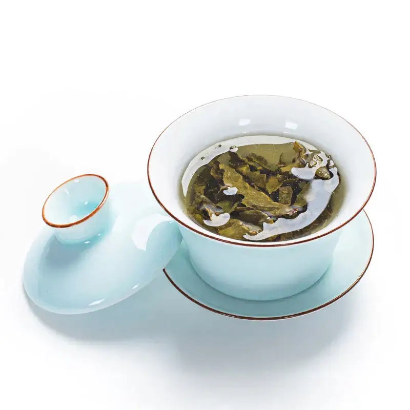A delicate celadon tea set featuring a light blue ceramic gaiwan with gold rim accents and matching lid and saucer