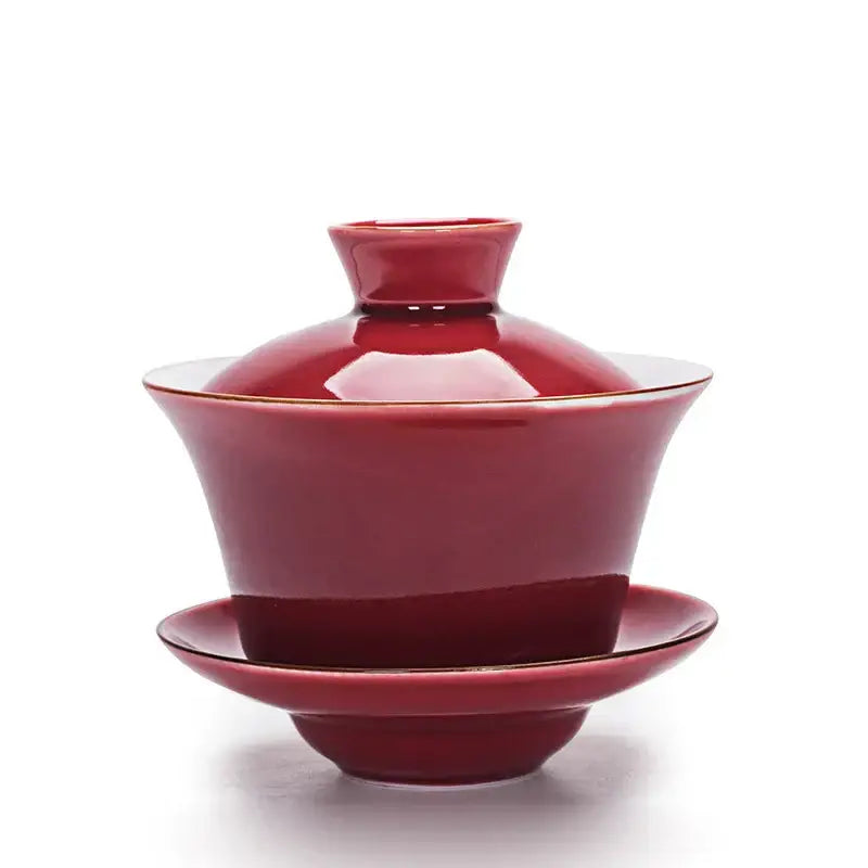 A glossy crimson ceramic gaiwan with gold trim paired with a celadon tea tureen tea set for dining rooms