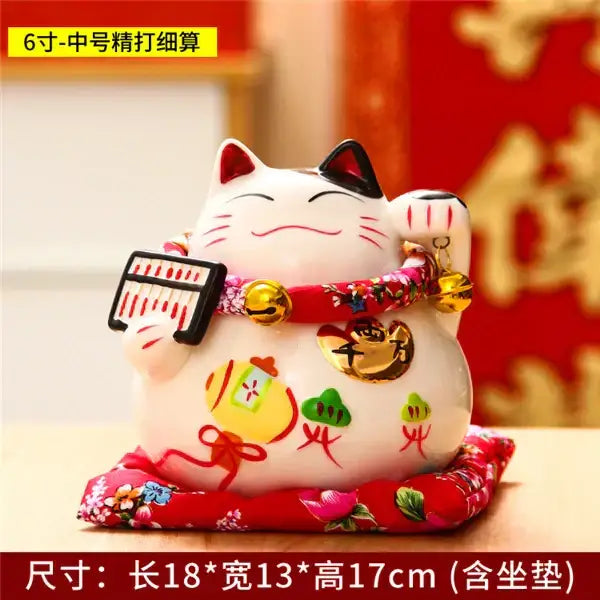 White ceramic maneki neko piggy bank with black accents red floral collar and gold bells holding a miniature keyboard decorbites ceramic maneki