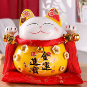 A cheerful white ceramic maneki neko piggy bank with yellow ears floral patterns red sash holding golden bells decorbites ceramic maneki