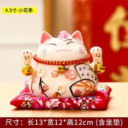 White ceramic maneki neko piggy bank with pink floral patterns red braided collar and golden bells for decorbites ceramic maneki decor