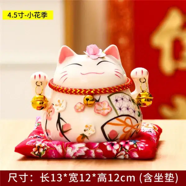 White ceramic maneki neko piggy bank with pink floral patterns red braided collar and golden bells for decorbites ceramic maneki decor