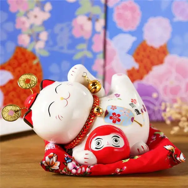 White ceramic maneki neko piggy bank with gold coins and bells on red cushion decorbites ceramic maneki decor