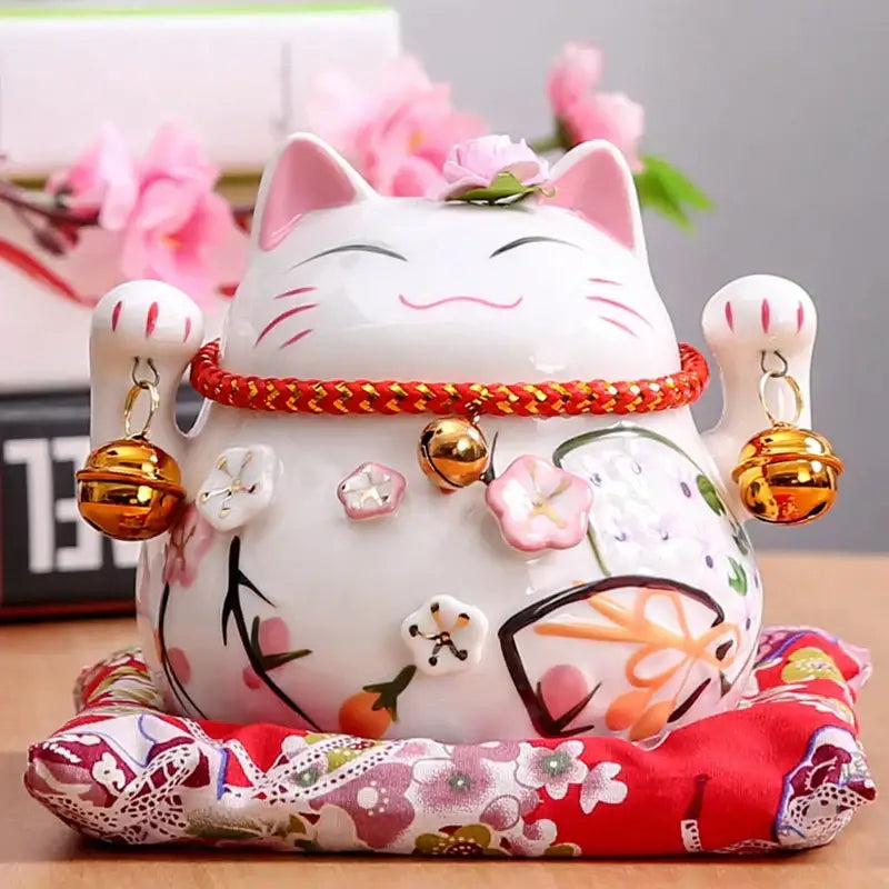 White ceramic maneki neko piggy bank with pink floral accents gold bells and red cord for decorbites ceramic maneki decor