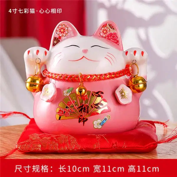 Pink ceramic maneki neko piggy bank with floral ear decorations gold bells and red cord by decorbites ceramic maneki