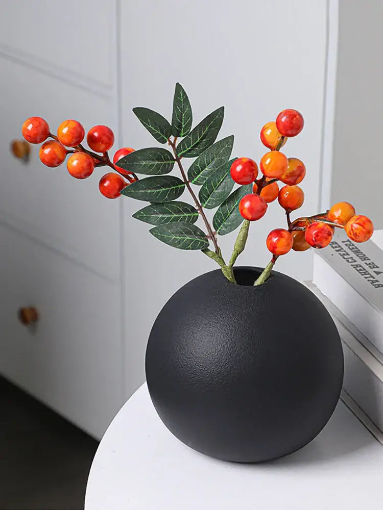 Black white ceramic round vase black white holding artificial branches with glossy orange red berries and green leaves