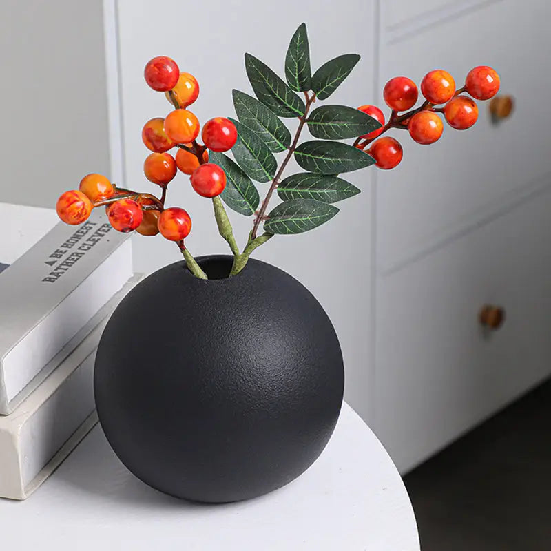 Black white ceramic round vase black matte holding artificial orange and red berries with green leaves