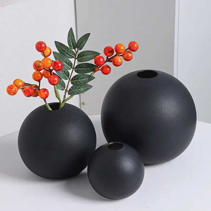 Set of three matte black ceramic round vases black white with one vase holding a branch with red and orange berries