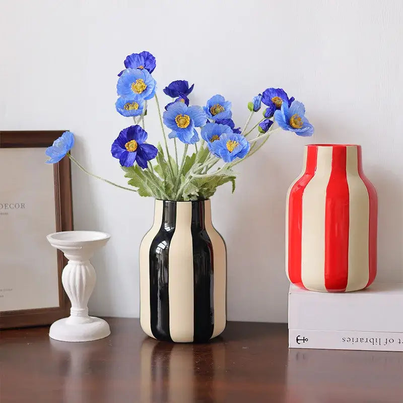 Black and cream striped ceramic vase holding blue poppies in a ceramic vase black red striped design