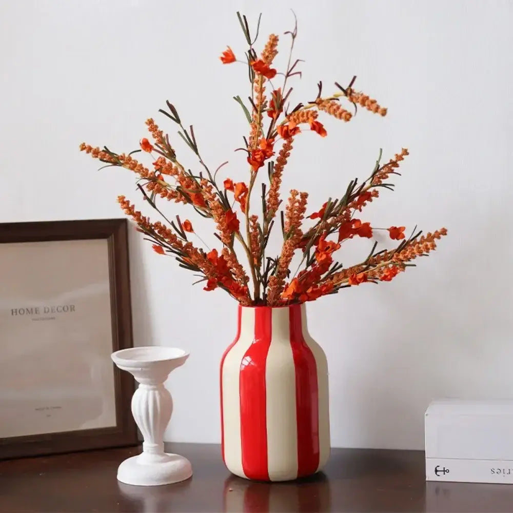 A glossy red and cream striped ceramic vase holding a bouquet of orange artificial flowers
