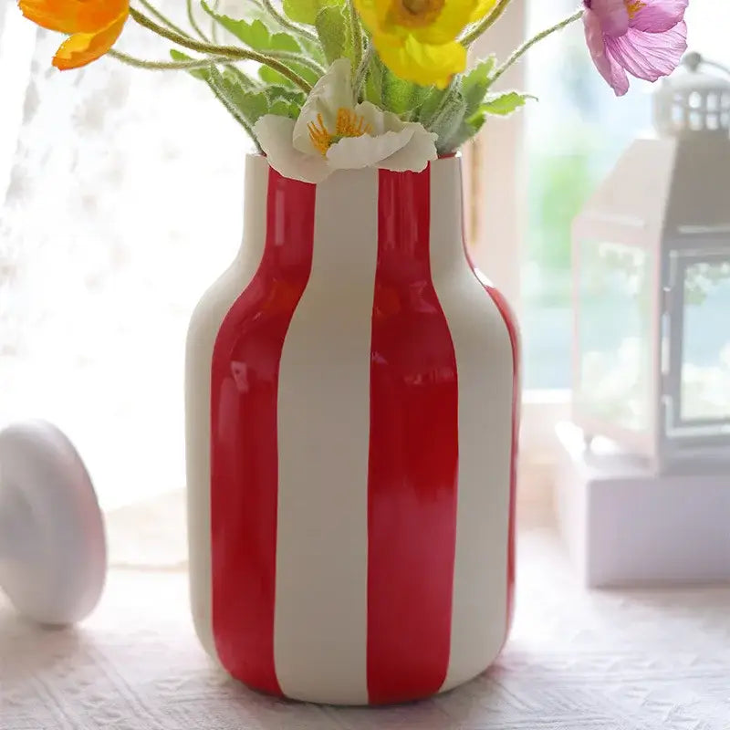 A glossy red striped ceramic vase with white vertical stripes holding a bouquet of artificial flowers