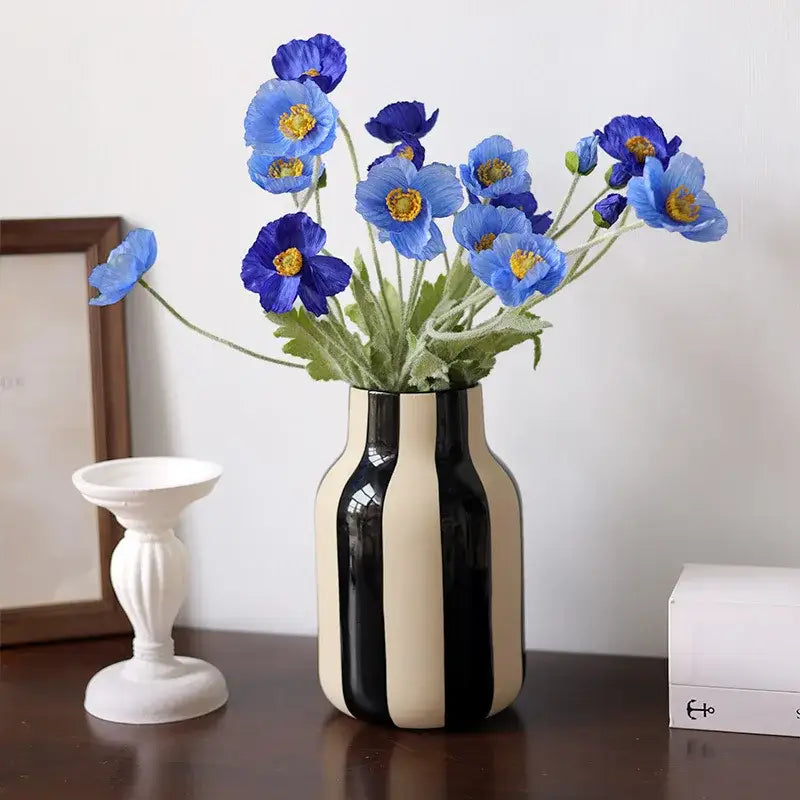 A sleek striped ceramic vase in black and cream holding artificial blue poppies for decorative use