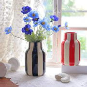 A sleek black and cream striped ceramic vase holding vibrant blue poppies in a red striped ceramic vase design