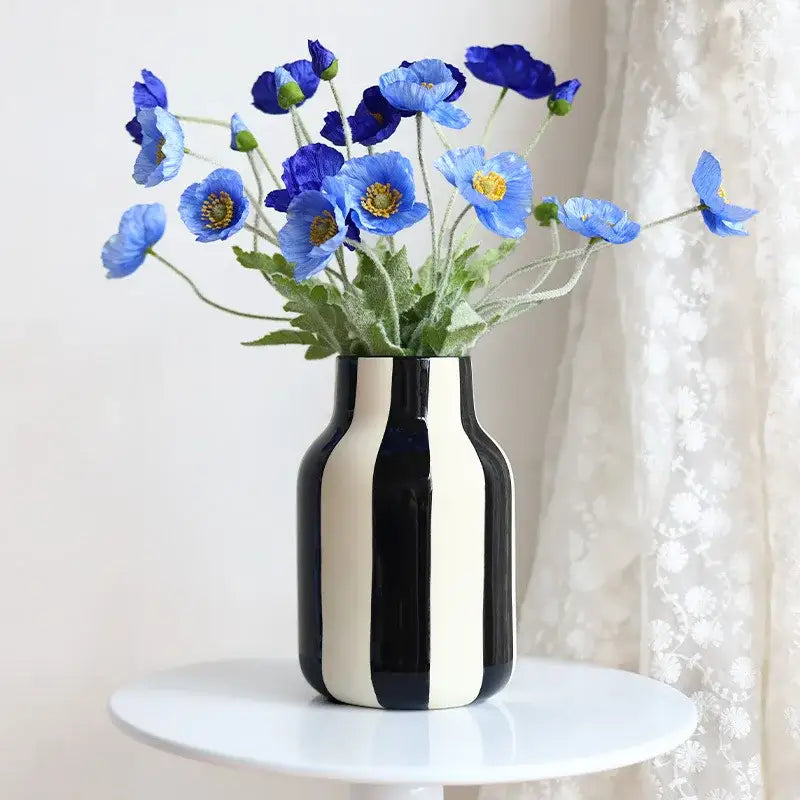 A sleek black and white striped ceramic vase holding vibrant blue poppies with yellow centers in a red striped design