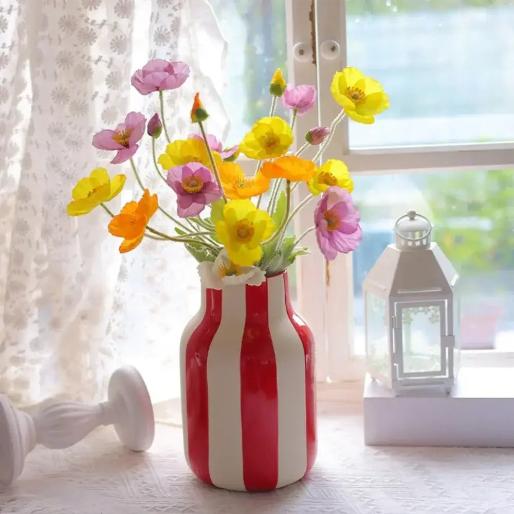 A red striped ceramic vase with vertical white stripes holding a bouquet of yellow pink and orange flowers