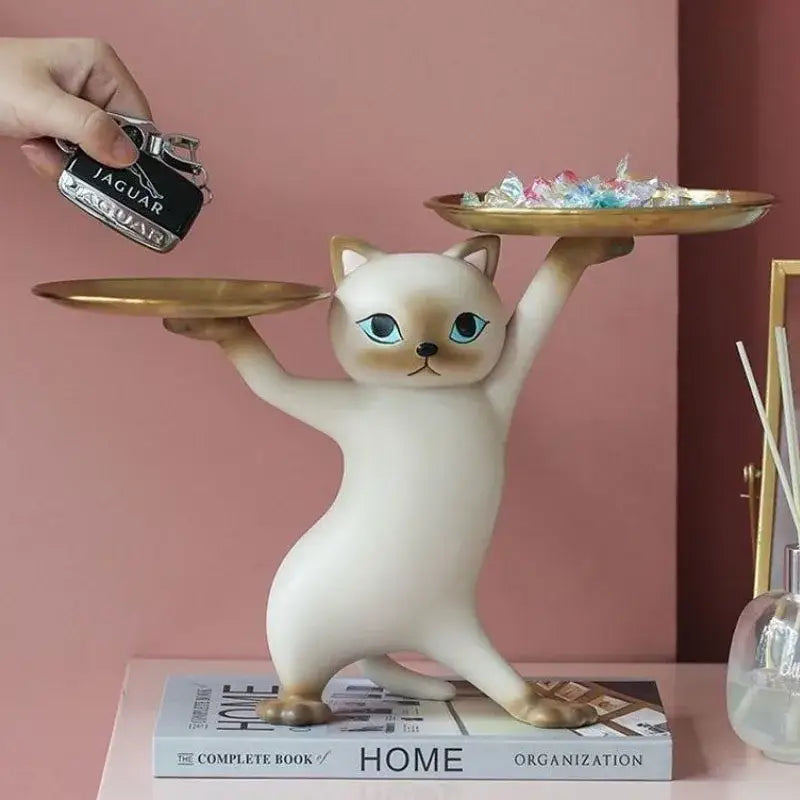 Cream-colored ceramic cat figurine with blue eyes balancing two gold trays as a cat figurines storage tray