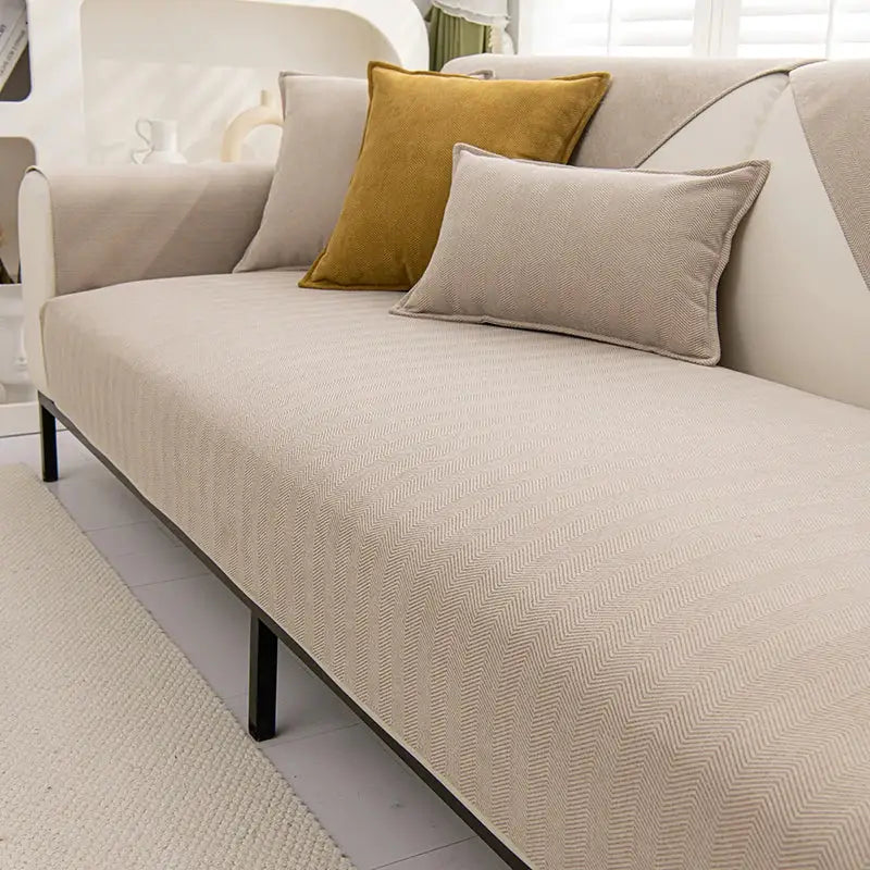 Beige chenille textured non-slip herringbone sofa cover with matching sofa cushions and black metal legs for living room use