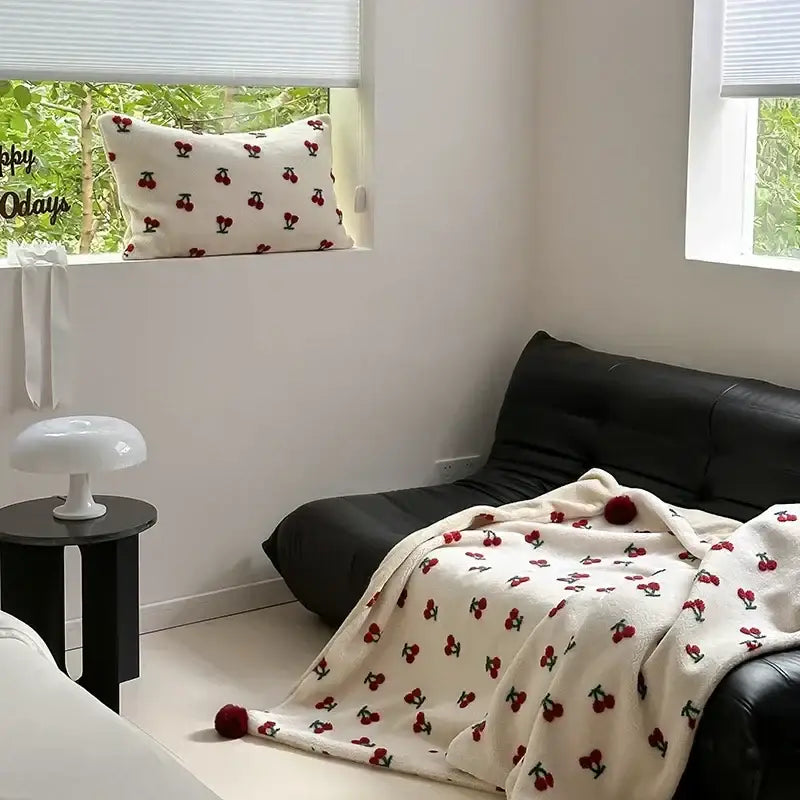 Cream-colored sheep rollie loop fleece blanket with red cherry embroidery and matching pom-pom tassels for bedroom use