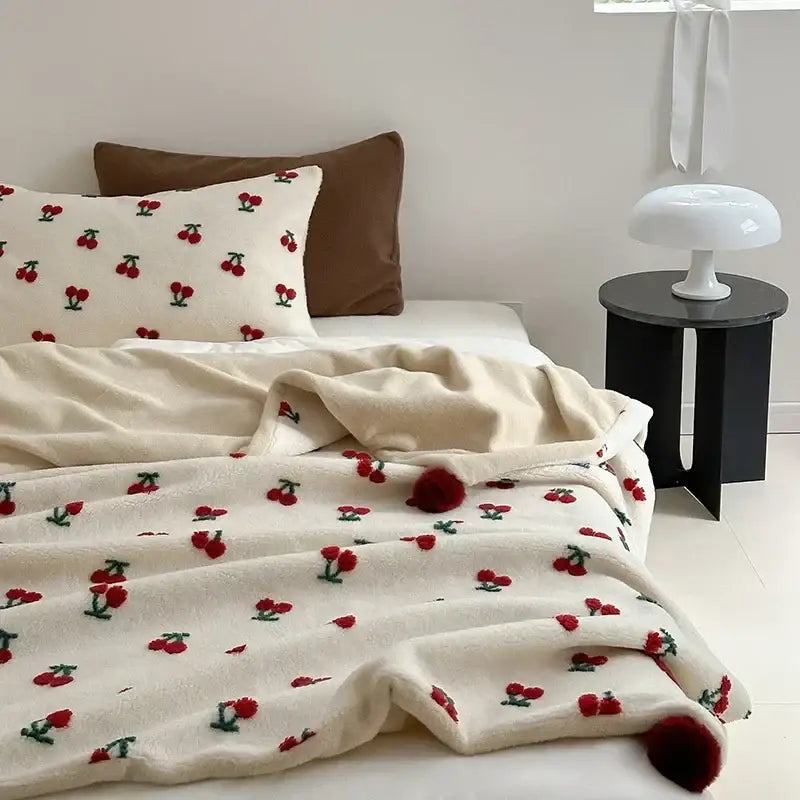 Cream-colored rollie loop fleece blanket with red cherry embroidery and matching pom-pom tassels sheep rollie design