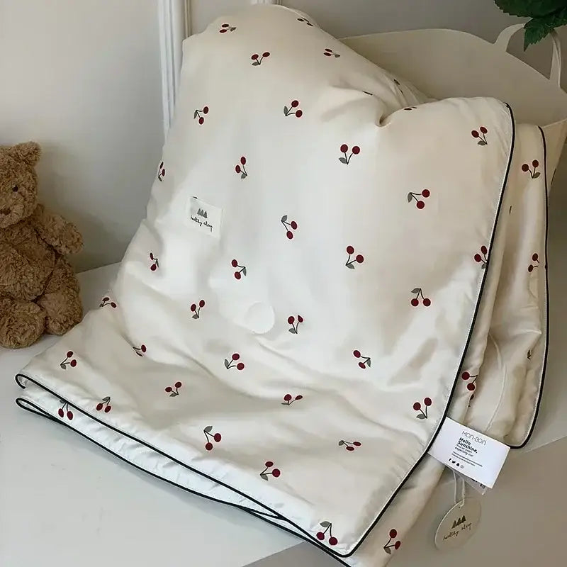 Cream-colored decorbites cooling quilt with red and green cherry embroidery and black piping edges for bedroom use