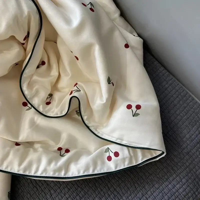 Cream-colored satin cooling quilt with embroidered red cherries green stems and dark green piping for night’s sleep
