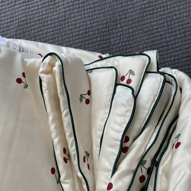 Cream-colored satin cooling quilt with red cherry embroidery and dark green piping from decorbites cooling quilt collection