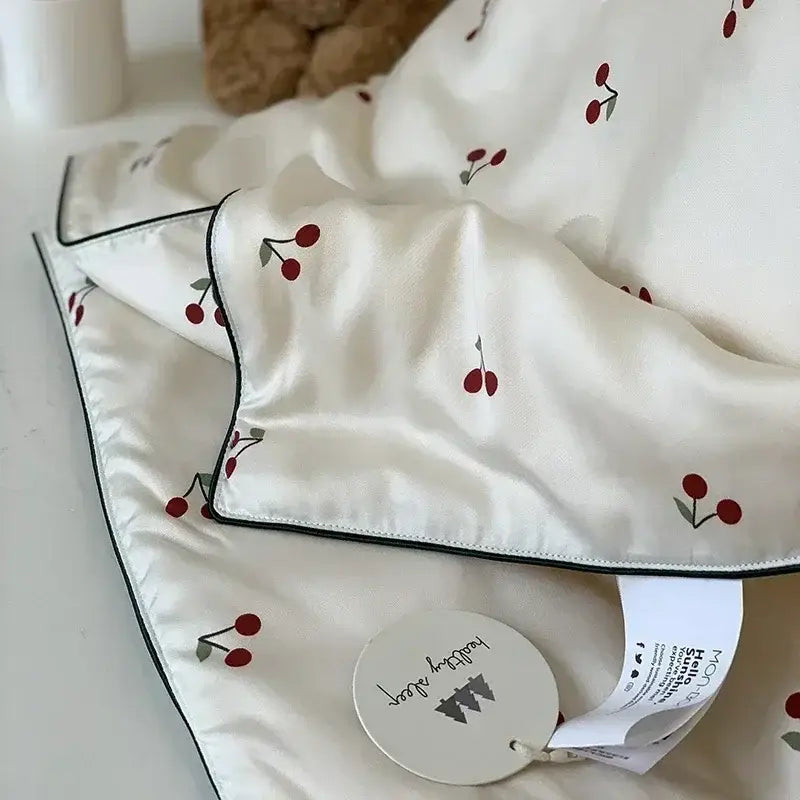 A soft white satin decorbites cooling quilt with red cherry embroidery and black piping edges for bedroom use