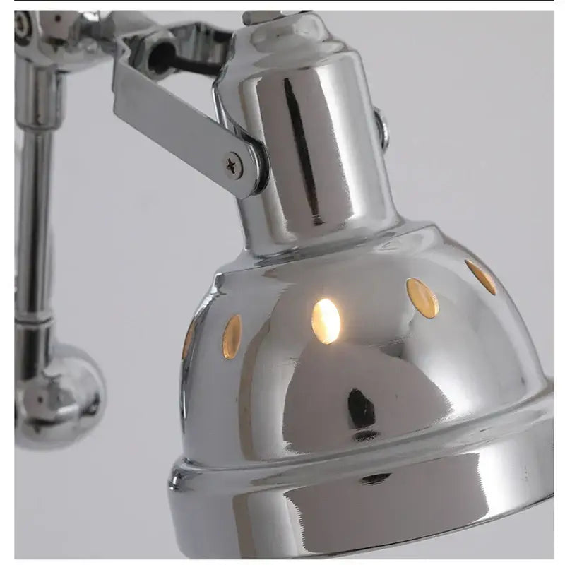 Chrome amber adjustable folding industrial wall light with chrome finish and dome shade featuring circular cutouts emitting warm light