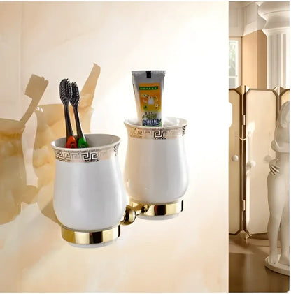 White ceramic toothbrush holder with gold trim and greek key pattern holding black toothbrushes in bathroom hardware set
