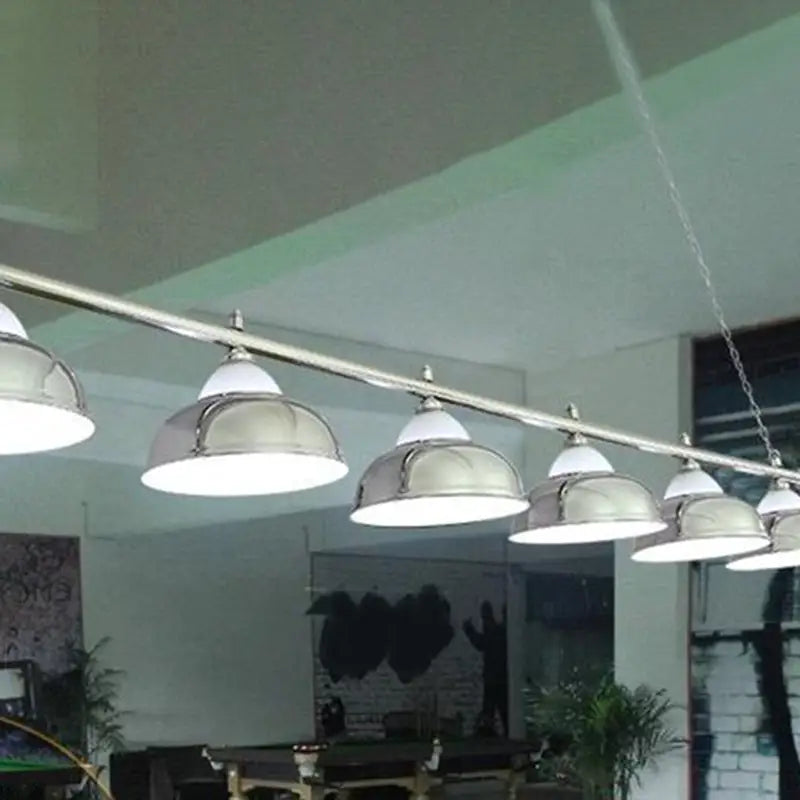 A row of silver stainless steel billiard dome lights with white interiors hang from a metallic bar for game room ceiling use