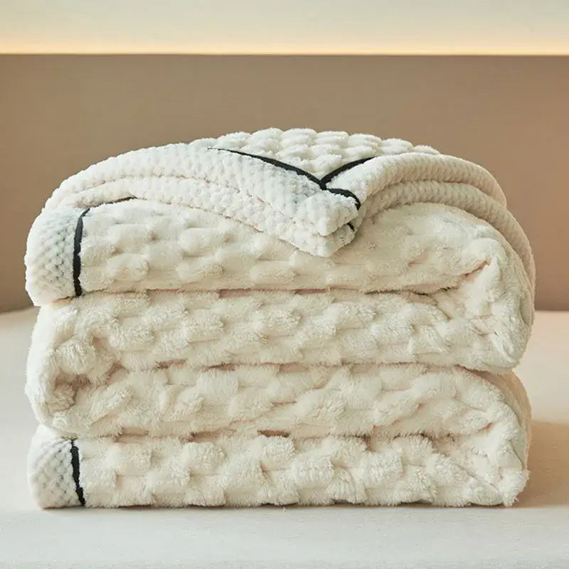A plush off-white coral fleece blanket with subtle black piping and a soft fuzzy surface for bedroom throw use